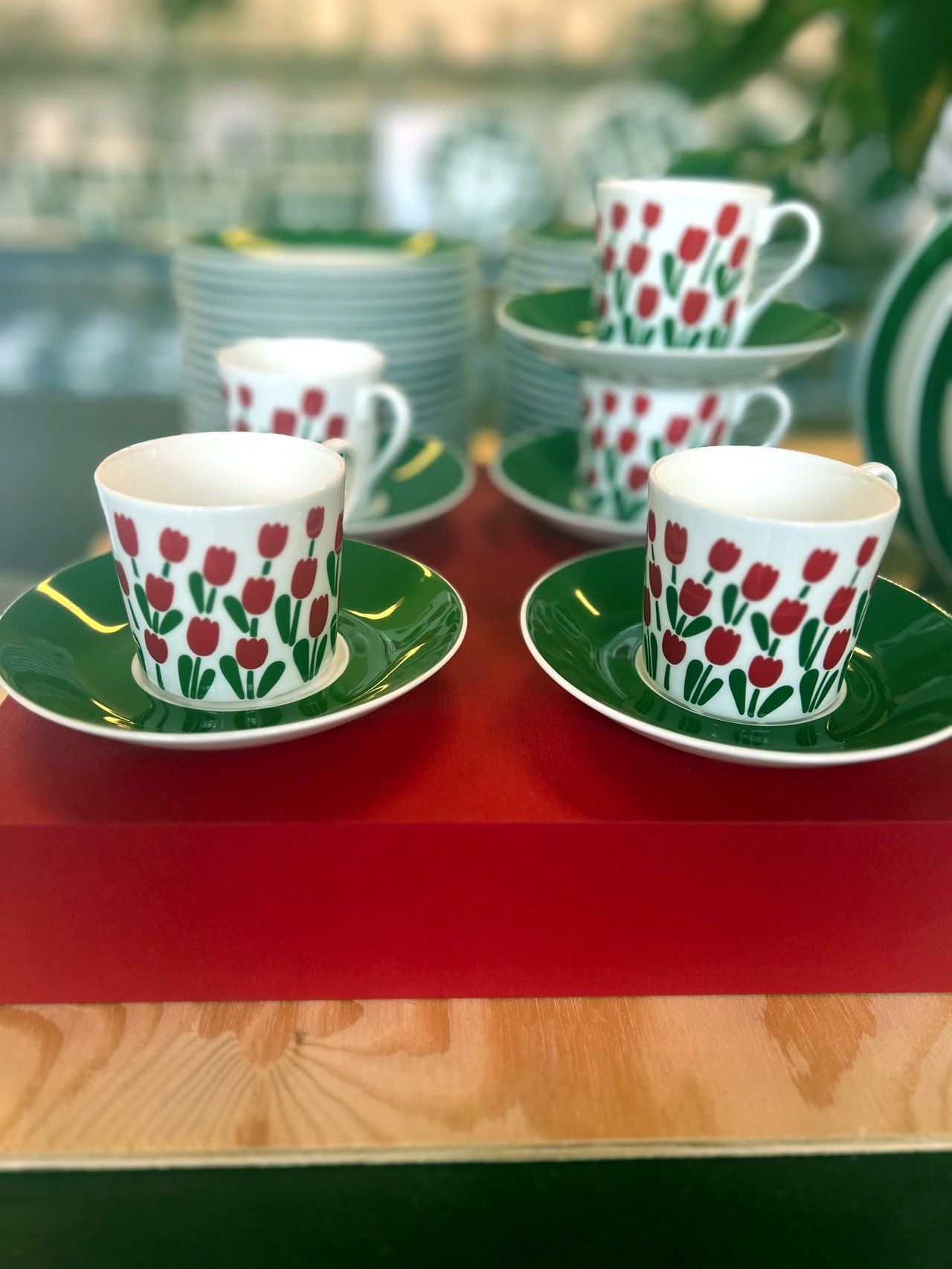 Coffee cups and saucers with red tulips and green rims on a red table
