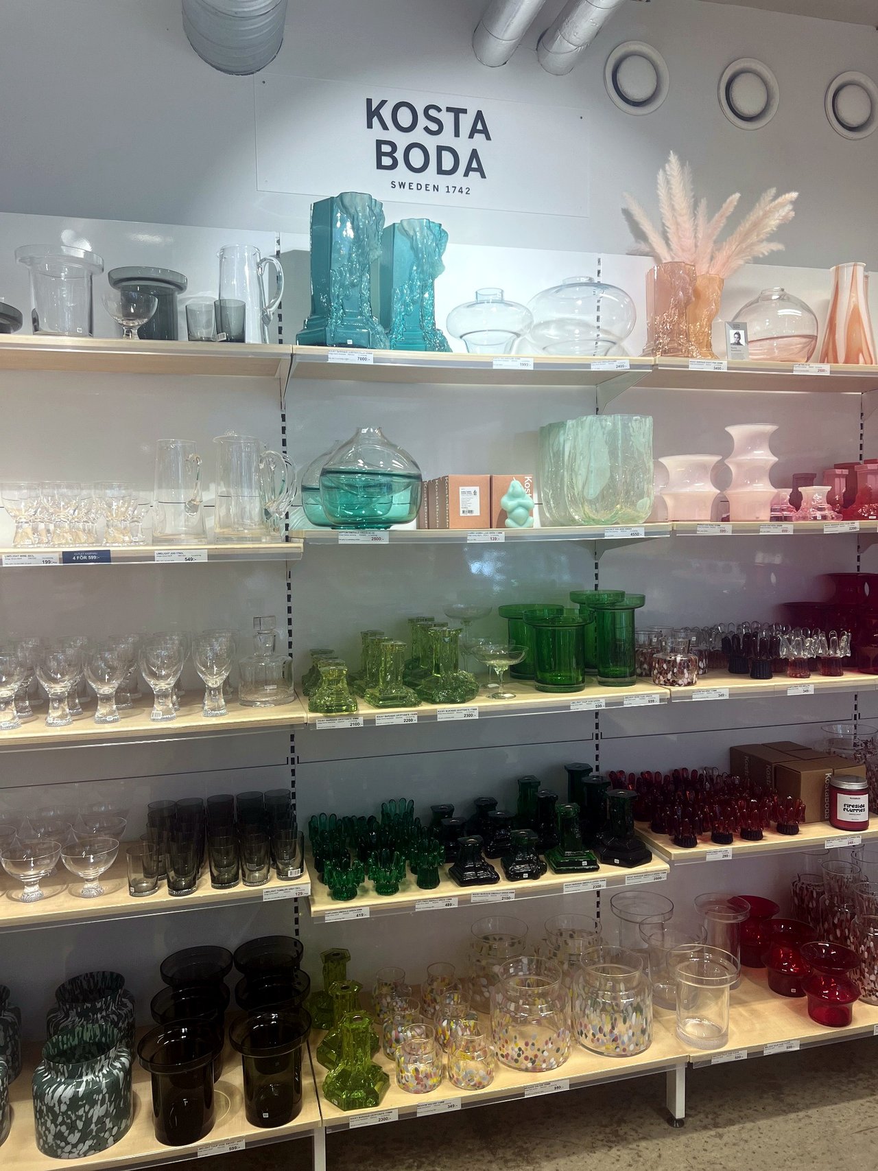 Shelves of coloured Kosta Boda art glass in turquoise, green, pink and red