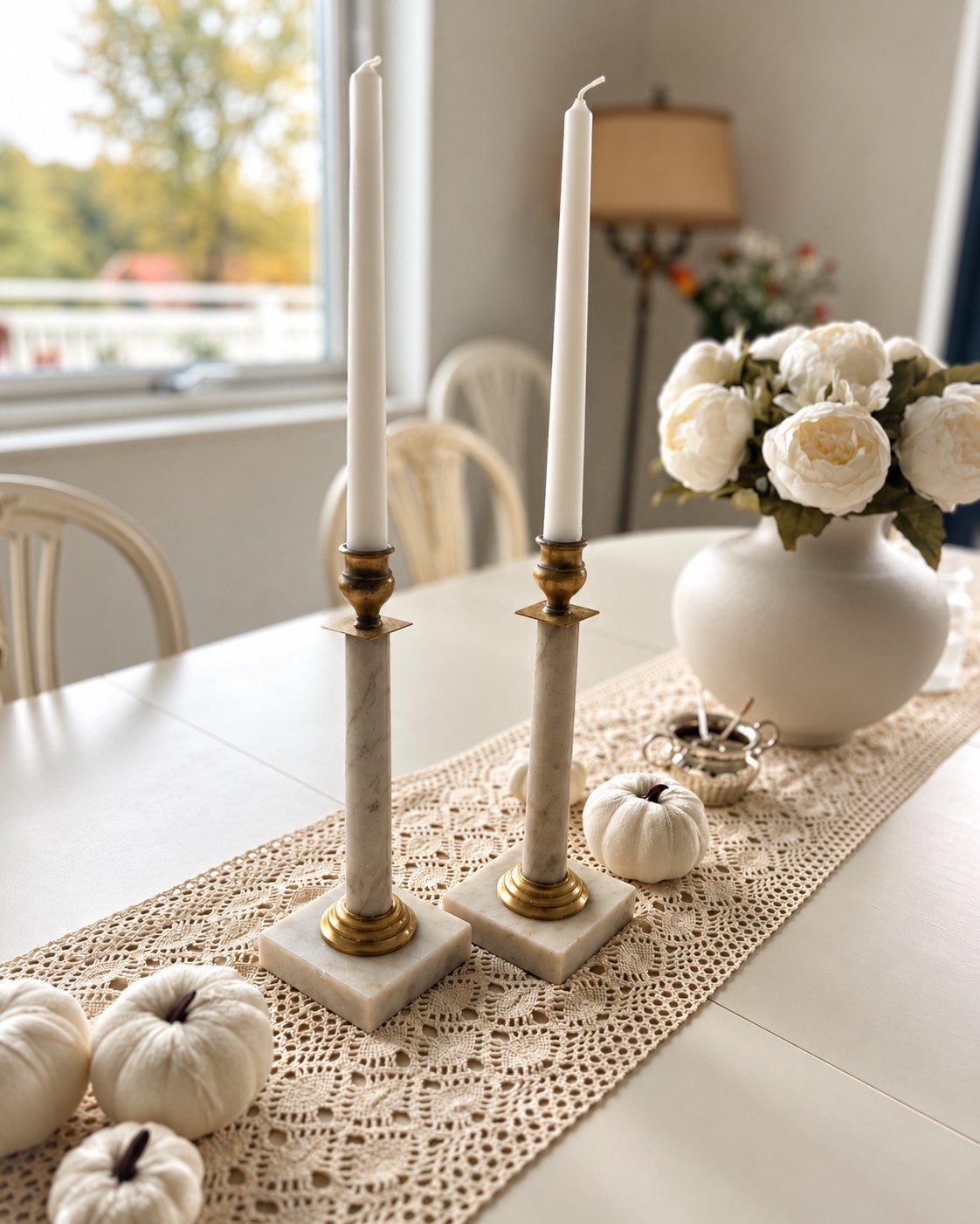 Two brass and marble candleholders on a crocheted runner beside a vase of white flowers