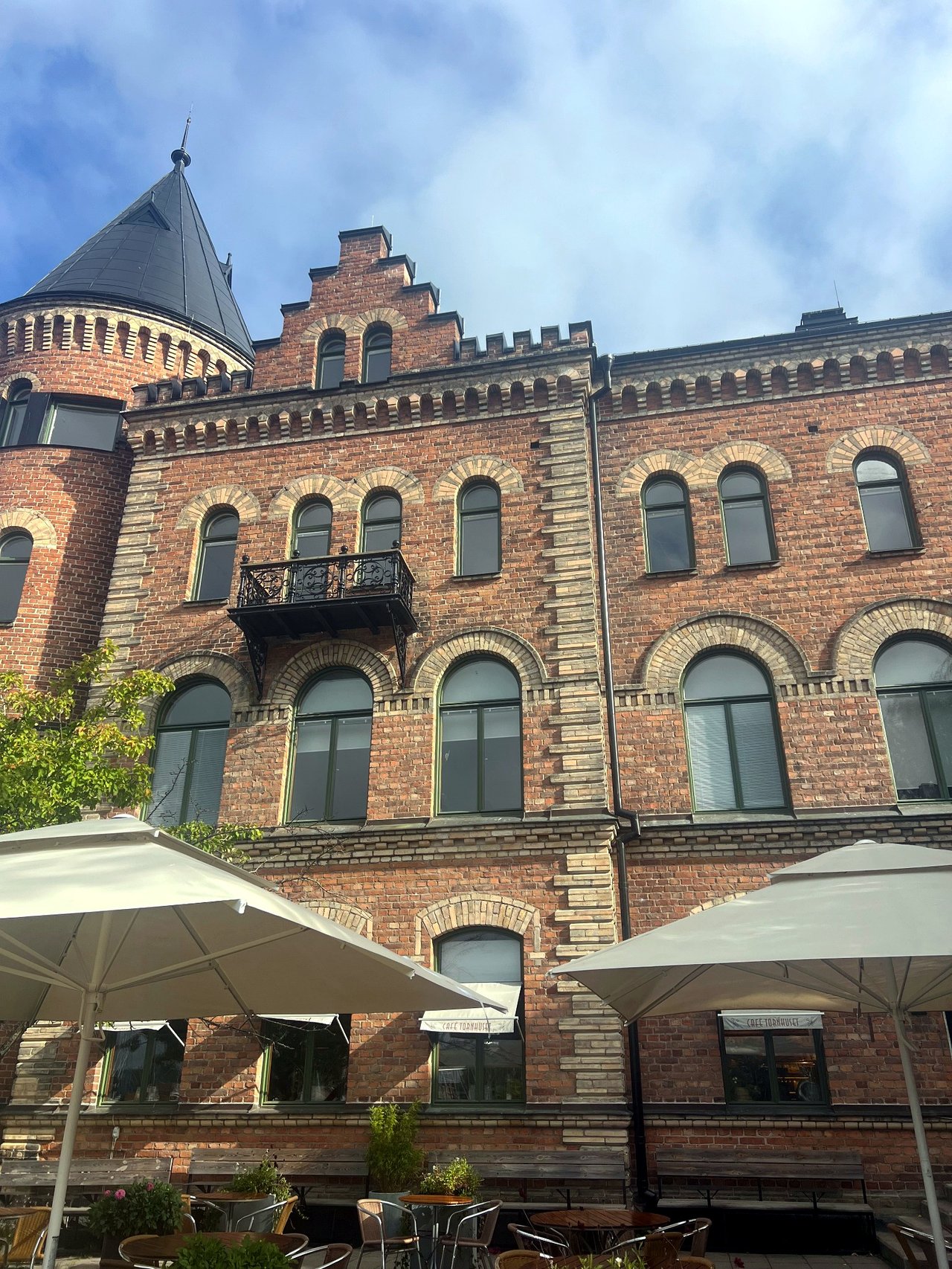 Historic brick building with stepped gables and a tower in Gustavsberg, with outdoor seating in the foreground