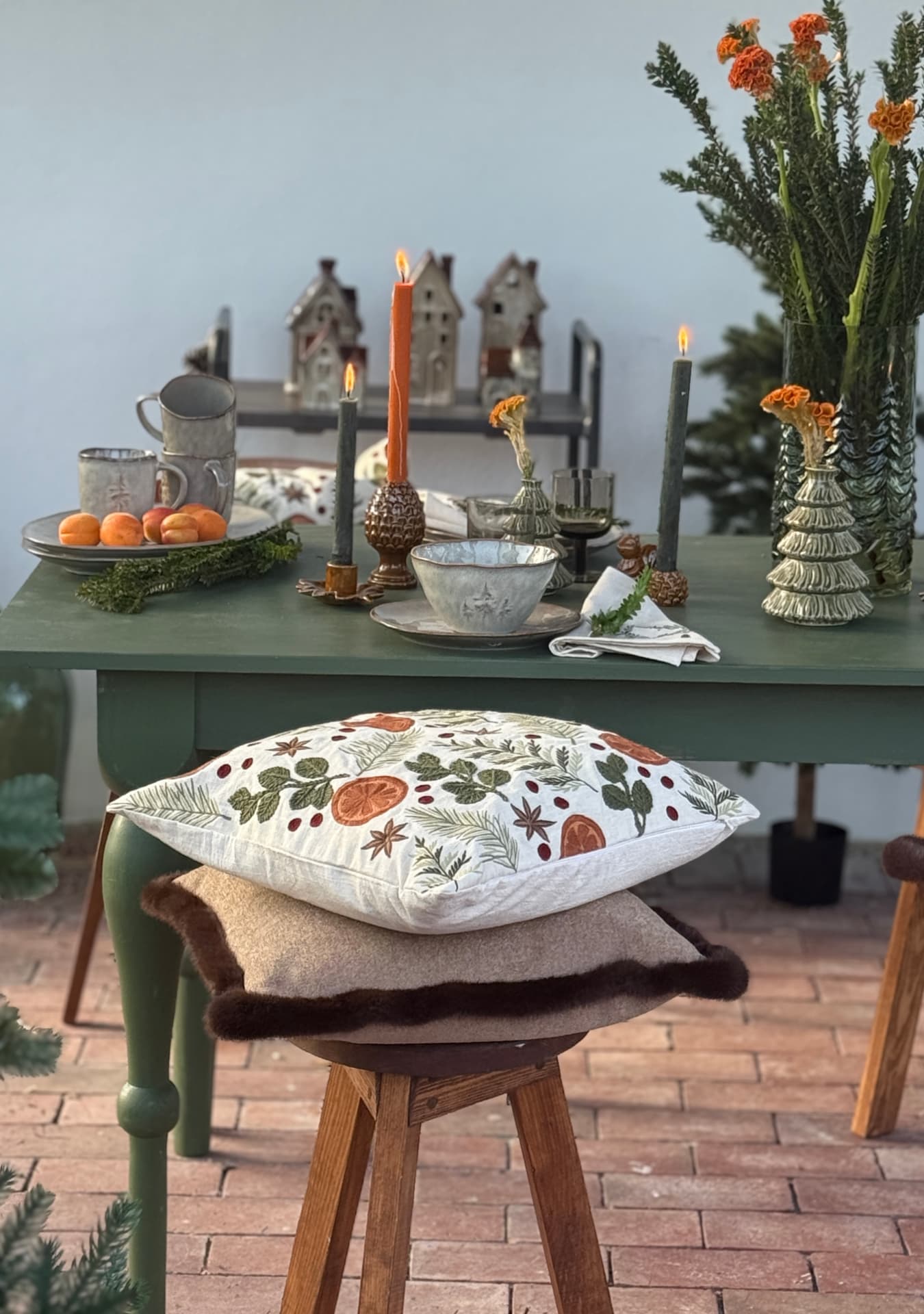 Green table set with ceramics, lit candles and an embroidered cushion on a stool