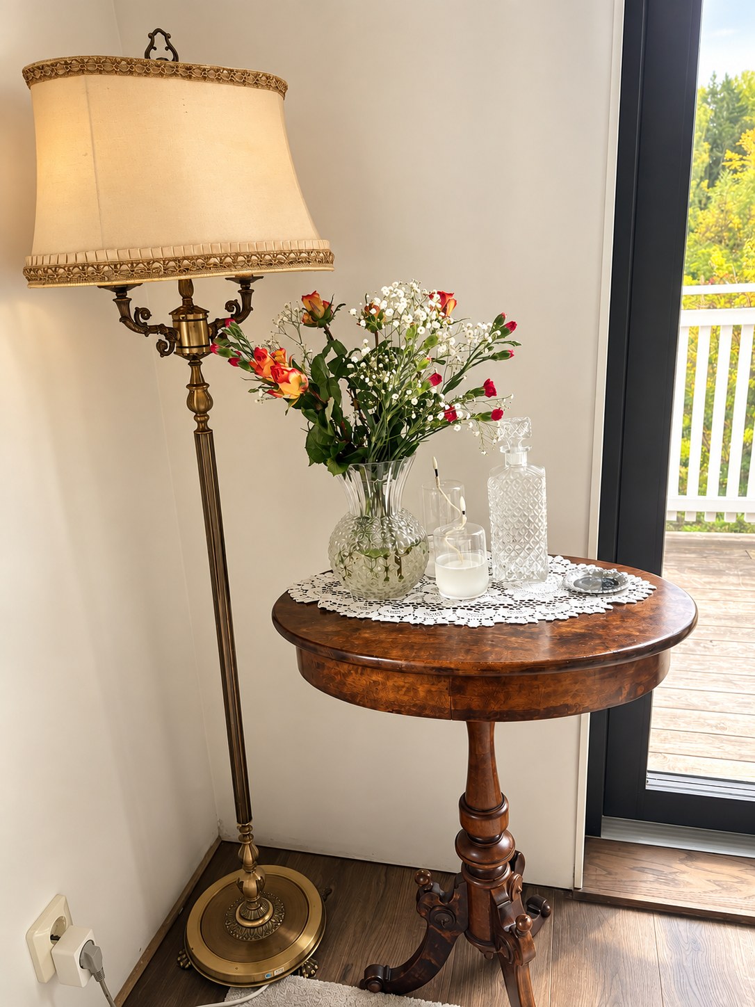 Inherited brass floor lamp with a fabric shade beside a small round wooden side table with flowers and a glass decanter