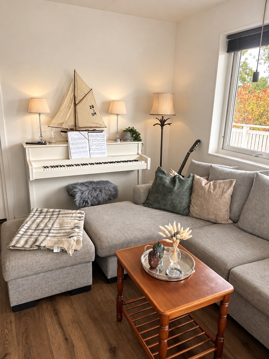 Older wooden coffee table with a silver tray in front of a grey corner sofa, with a white piano and a model sailboat behind