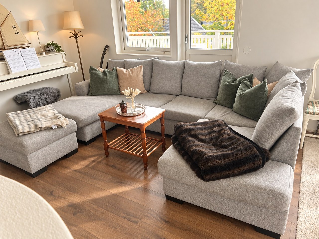 Bright living room with a grey corner sofa, an older wooden coffee table and a white piano by the window