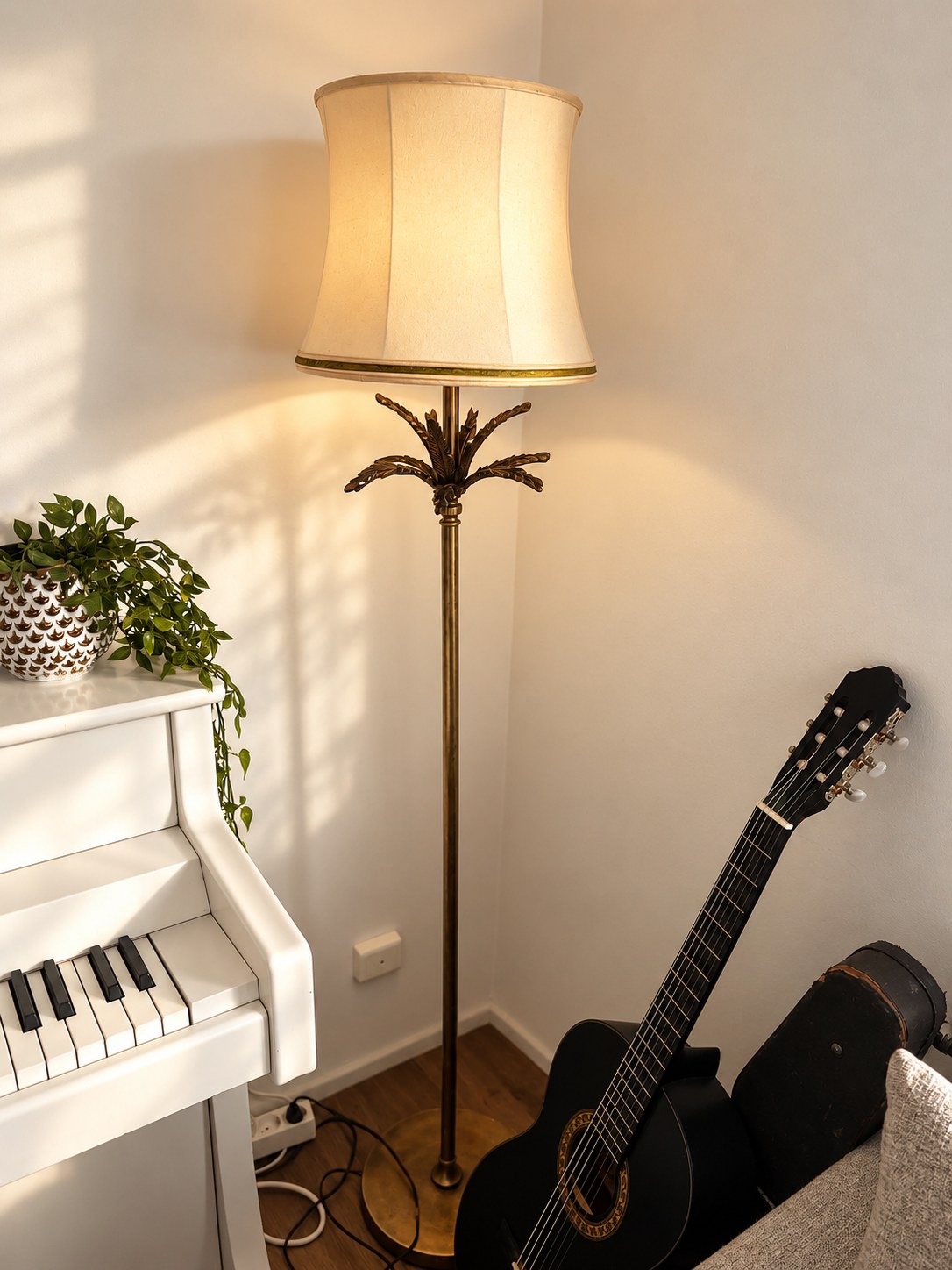 Floor lamp with a palm-shaped stem beside a white piano and a black guitar