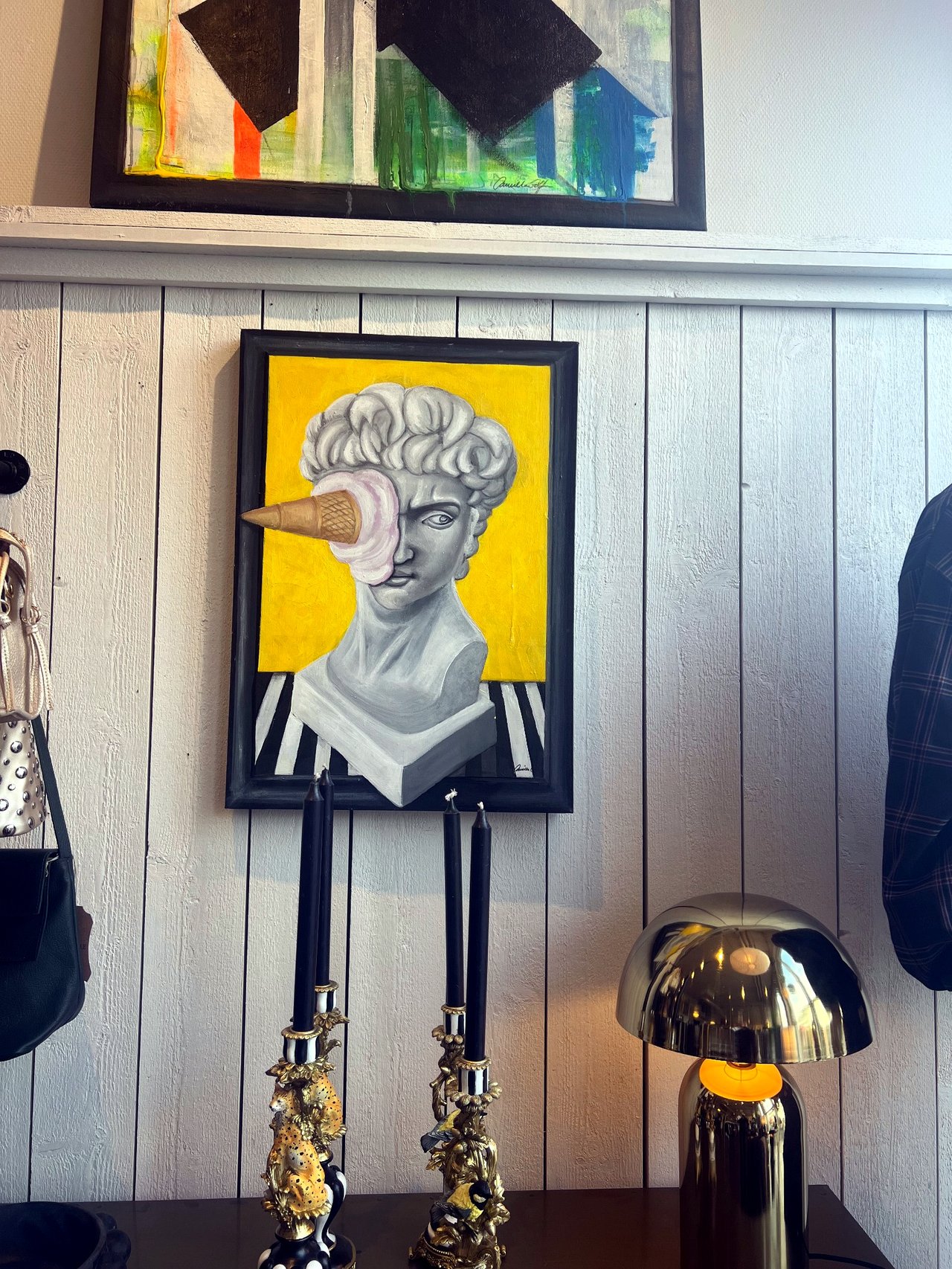 Painting of a bust against a yellow background above a polished brass lamp and tall candlesticks